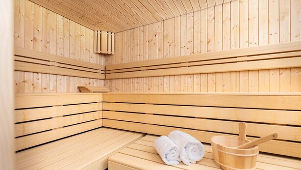 Een sauna met houten banken en een bankje met handdoeken en een houten emmer.