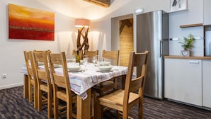 Een eetruimte met een tafel voor zes personen, houten stoelen, een moderne keuken met een roestvrijstalen koelkast, en een schilderij aan de muur.