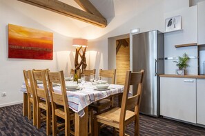 A dining area with a table set for six, wooden chairs, a modern kitchen with a stainless steel refrigerator, and a painting on the wall. - Chalet in Paradiski With Spa & Valley Views (Peisey-Nancroix)
