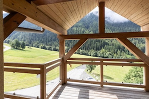 A wooden balcony with a view of a green landscape and a road. - Chalet in Paradiski With Spa & Valley Views (Peisey-Nancroix)