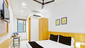 A hotel room with a bed, bedside table, desk, chair, wardrobe, ceiling fan, air conditioning unit, window, and artwork on the wall. - Super Hotel O Raipur (Raipur)