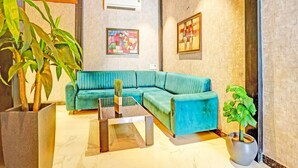 A modern living room with a teal sofa, a coffee table, a potted plant, and artwork on the walls. - Super Hotel O Raipur (Raipur)