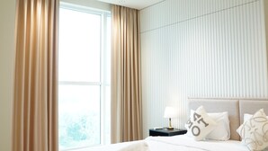 Habitación de hotel moderna con una cama grande, una mesita de noche, una ventana con cortinas e iluminación empotrada en el techo.