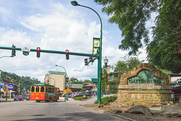 A street with a trolley, a stone sign reading 'Gatlinburg,' and a green streetlight. - 🏔 Baskins Creek 502 - Cozy Condo Steps from Downtown | Private Balcony🏔 (Gatlinburg)