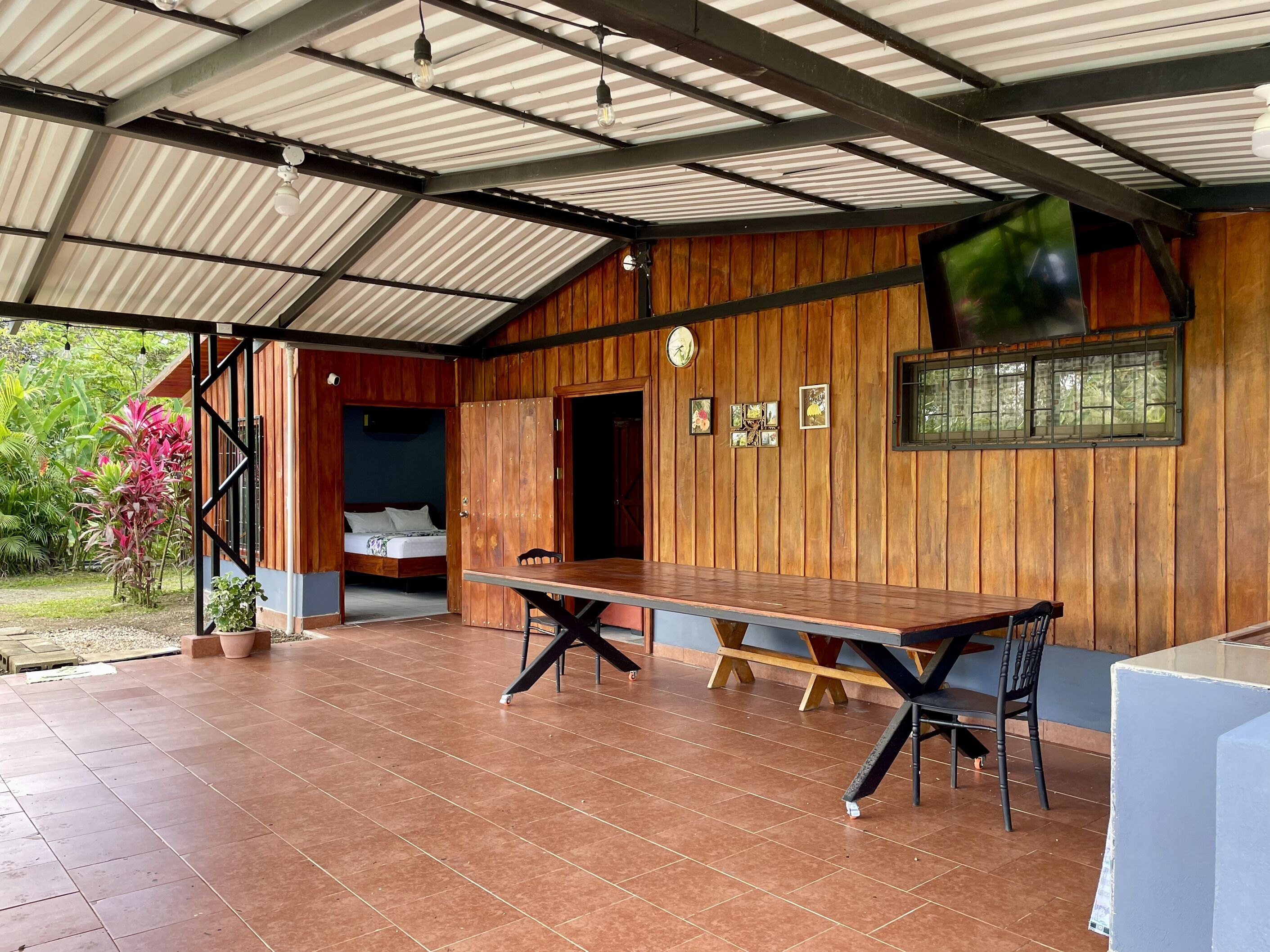 Una veranda riparata con tavolo e sedie in legno, un letto con vista e un orologio appeso al muro.