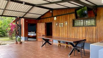 Una veranda riparata con tavolo e sedie in legno, un letto con vista e un orologio appeso al muro.