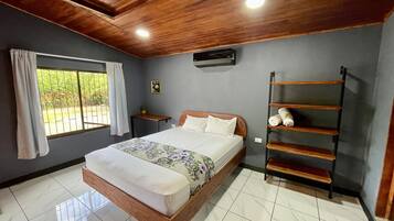 A bedroom with a bed, a window with curtains, a wall-mounted air conditioner, and a wooden shelf.