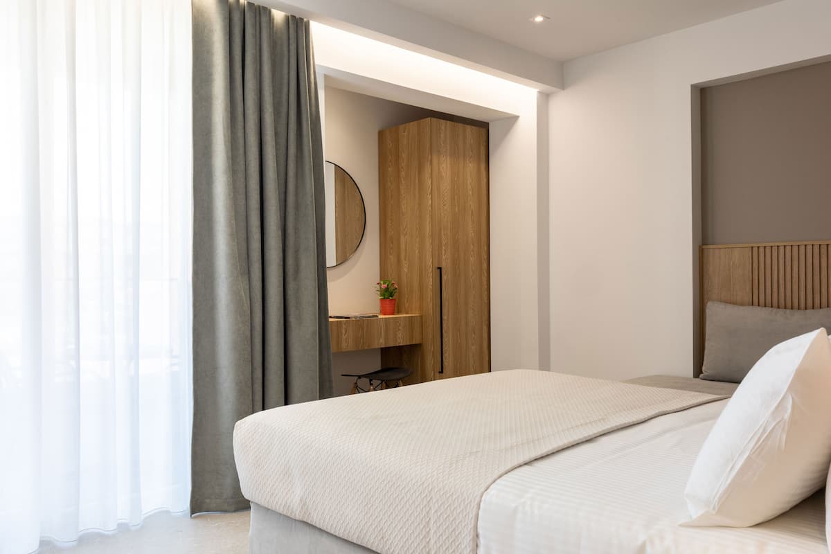 Un dormitorio moderno con una cama, un armario de madera, un espejo redondo y una pequeña mesa con una planta.