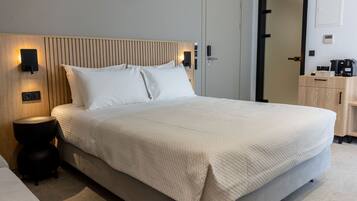 Una cama bien hecha con cabecera, lámparas de noche, una mesita redonda y un aparador de madera.