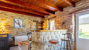 Un espace bar aux murs de pierre, doté de tabourets, d’un plafond en bois et offrant une vue à travers une porte.