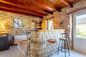 Eine Bar mit Steinwänden, Sitzhocker, Holzbalkendecke und Blick durch eine Tür.