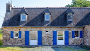 Un bâtiment en pierre avec un toit en pente, de nombreuses fenêtres et des volets bleus.