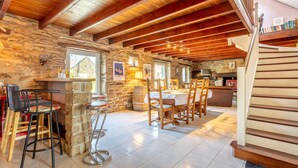 Un intérieur rustique avec des murs en pierre, des poutres en bois, un coin bar et un escalier.
