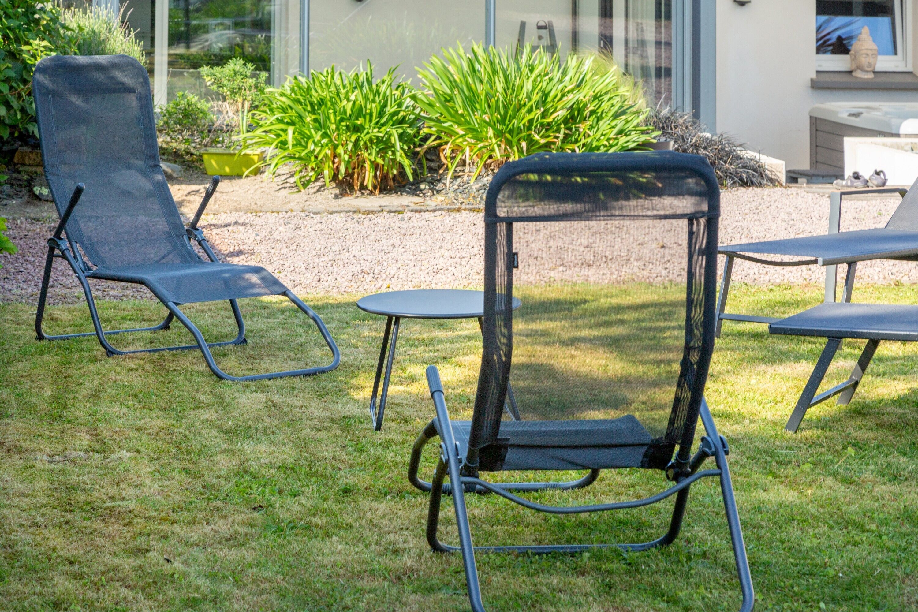 Dos sillones de exterior con estructura metálica y respaldo de malla, ubicados sobre un césped con un sendero de grava y follaje al fondo.