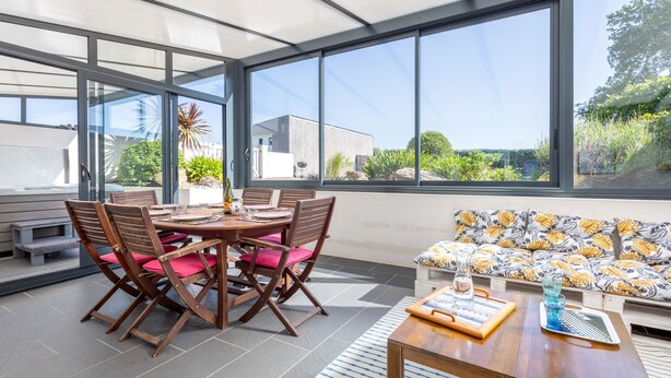 Une terrasse ensoleillée avec une table à manger, des chaises et un canapé.