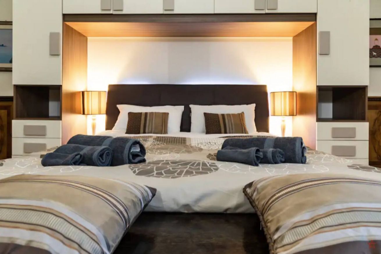 Una camera d'albergo con un letto grande, due abat-jour e un poggiatesta illuminato.