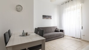A modern living space with a dining table, chairs, a sofa, a wall clock, a cityscape picture, and sheer curtains. - Fiera Milano - Total Relax Pero is a cozy and functional apartment, ideal for those seeking tranquility and comfort.Located just minutes from Fiera Milano Rho and well connected to the center of Milan, it offers well-kept rooms, equipped kitchen and comf (Pero)