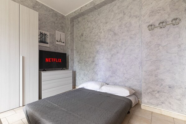 A bedroom with a bed, a wardrobe, a TV, and a wall-mounted shelf.
