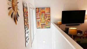 A hallway with a staircase, a flat-screen TV, and wall art.