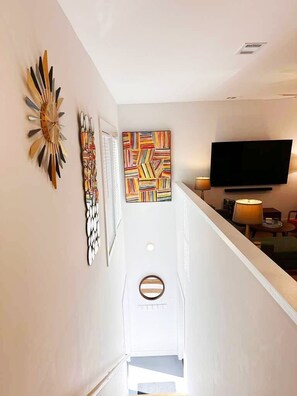 Ein Flur mit Treppe, einem Flachbildfernseher und Wandbildern.