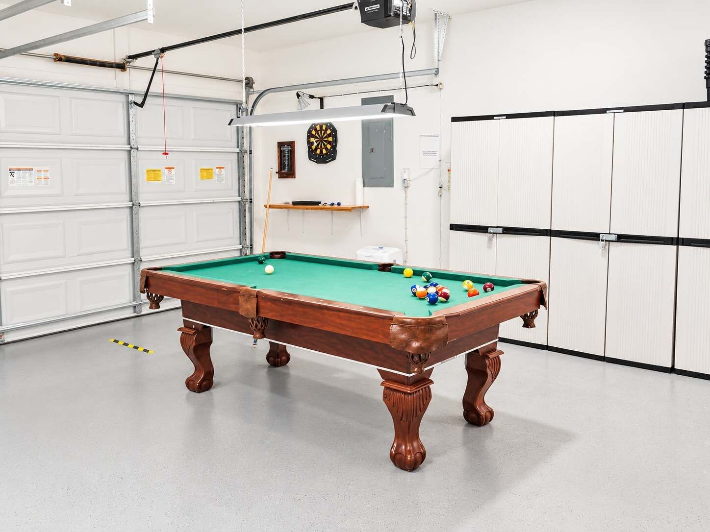 Ein Billardtisch in einer Garage, inklusive Dartscheibe und Regalen.