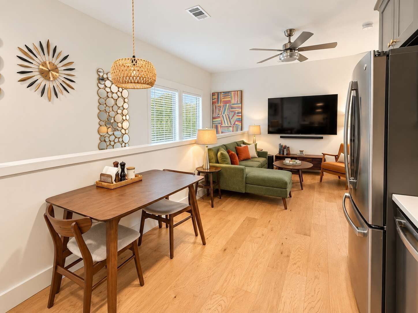 A modern kitchen with a dining area, a sofa, a TV, and a ceiling fan.