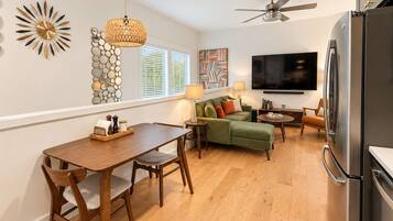 A modern kitchen with a dining area, a sofa, a TV, and a ceiling fan.