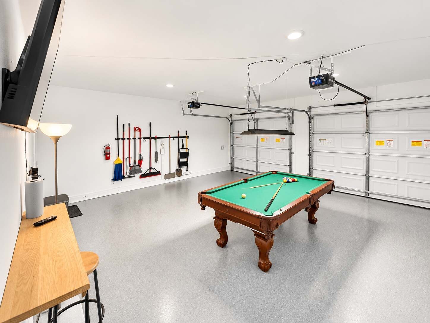 A billiards room with a pool table, a television, and various cleaning tools on the wall.