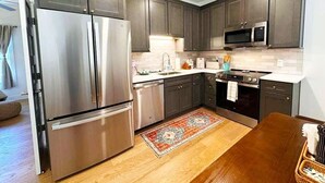 A modern kitchen with stainless steel appliances, dark cabinetry, and a patterned rug.