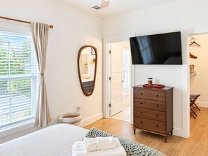 A bedroom with a bed, a dresser, a television, a mirror, and a window with curtains. - Savannah Victorian Escape w/ Game Room & Firepit (Savannah)