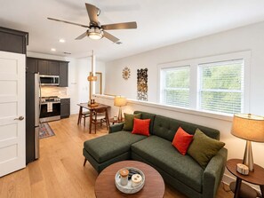 A modern living room with a sectional sofa, a dining table, and a kitchen area with a microwave. - Savannah Victorian Escape w/ Game Room & Firepit (Savannah)