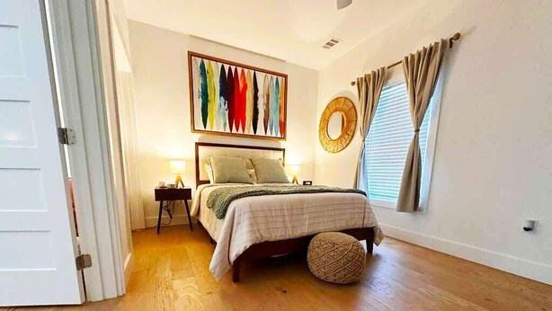 A bedroom with a bed, bedside table, lamp, and a wall-mounted mirror.