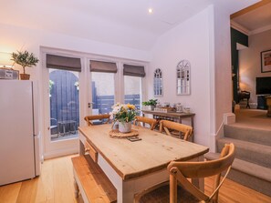 A dining area with a wooden table, chairs, and a bench. There is a window with blinds, a door leading outside, and a small table with decorative items. - Stylish Town Apartment (Ross-on-Wye)