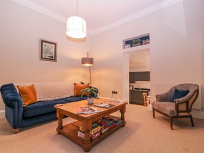 A living room with a sofa, a coffee table with books, a lamp, and a chair. - Stylish Town Apartment (Ross-on-Wye)