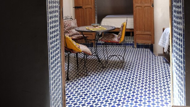 Una habitación con piso a cuadros, una araña, una cama y una mesa con sillas.