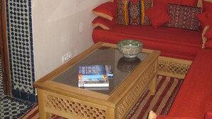 Una sala de estar con un sofá rojo, una mesa de centro de vidrio con un libro, azulejos de pared estampados y un cuadro enmarcado.
