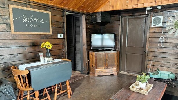 Ein Holzinterieur mit einem freundlichen Willkommensschild, einem Fernseher, einem Tisch mit Stühlen und einer kleinen Pflanze.