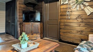 Ein Holzblockhaus-Innenraum mit einem Fernseher auf einem Schrank, einem Wandventilator und einem gewebten Korb mit einer Pflanze.