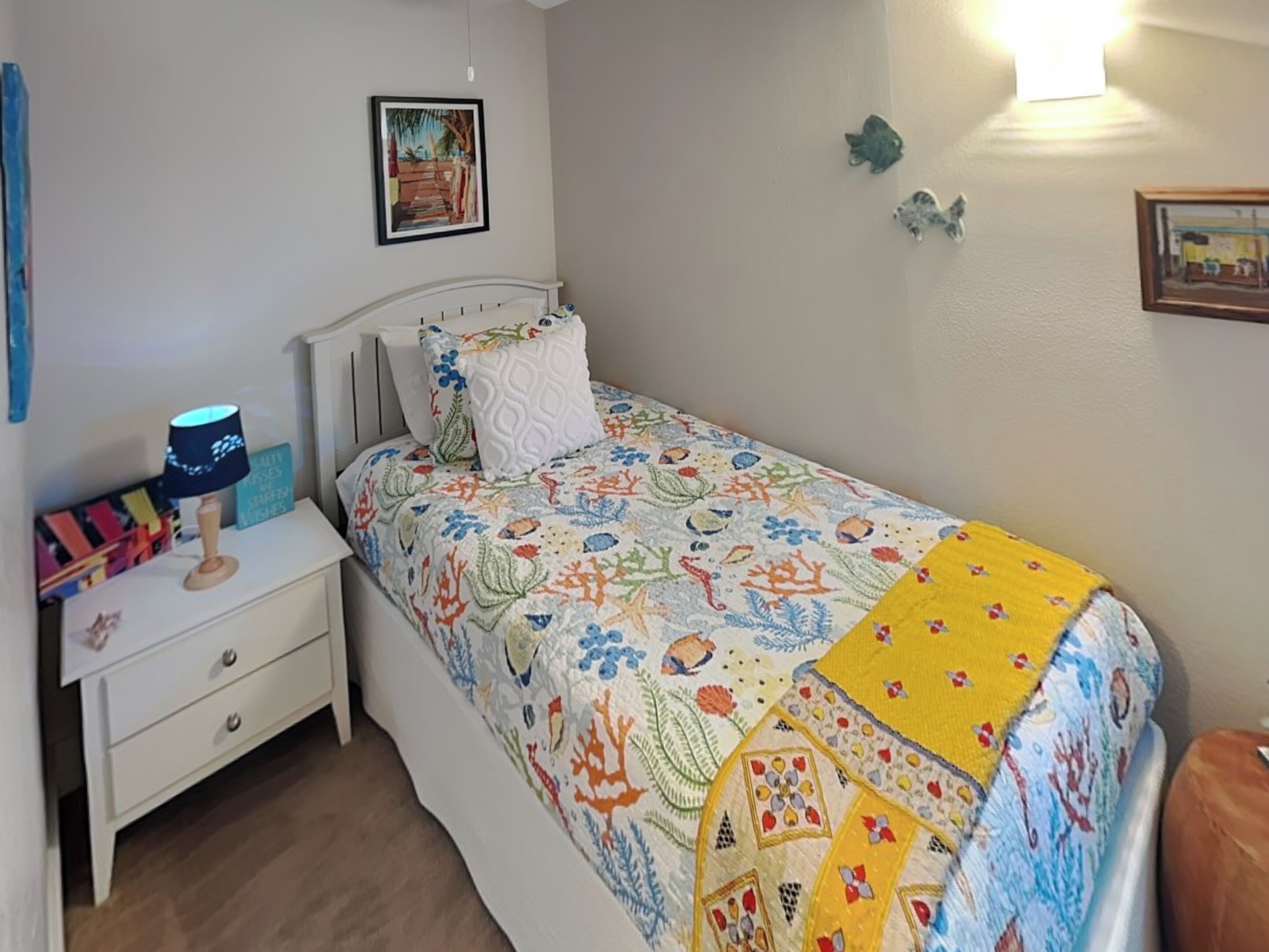 Een slaapkamer met een bed, een nachtkastje, een lamp, een lijst met een afbeelding aan de muur, en een klein plankje met decoratieve objecten.