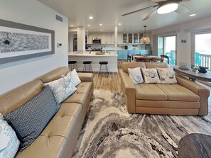 Un salon moderne avec un canapé beige, un tapis à motifs et une cuisine en arrière-plan.