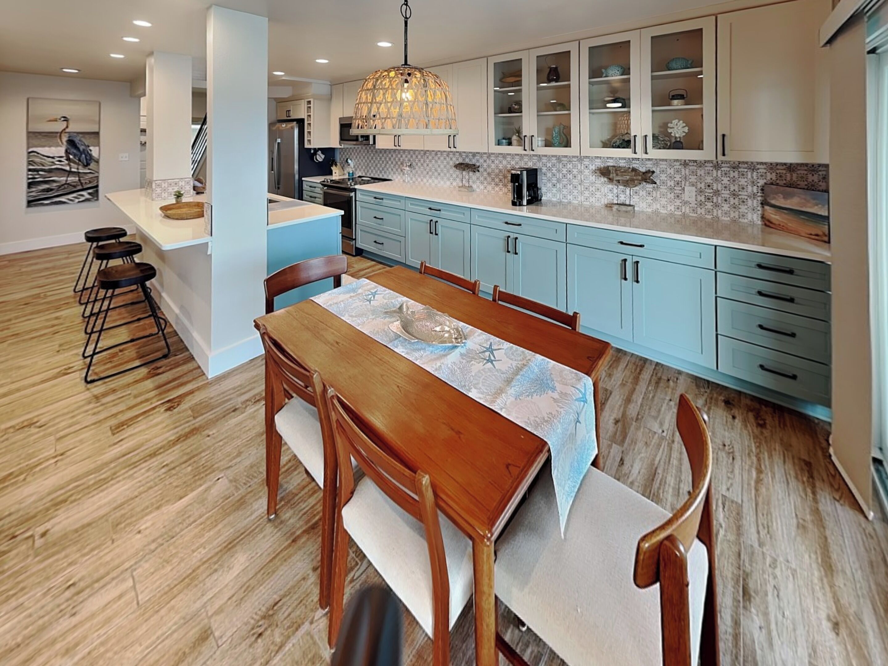 A modern kitchen with light blue cabinets, a wooden dining table, and a hanging pendant light.