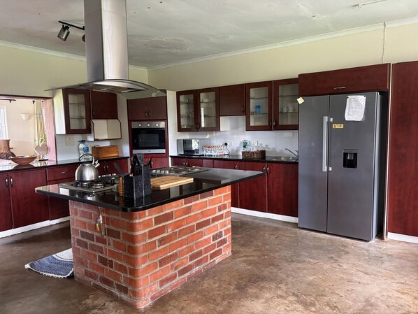 A kitchen with a central island, a refrigerator, and wooden cabinets. - Budget Double Room Mt Pleasant Heights - 2379 (Harare)