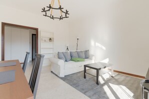 A living room with a white sofa, a small table, a chandelier, and a bookshelf. - GuestHost - Spacious 100m2 flat, ideal for up to 6 people, located on the fourth floor of a building with lift.The apartment is located in the Zara district, a key & well-connected area that connects the residential and commercial area of ​​Viale Zar (Milan)