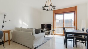 Een woonkamer met een bank, televisie, eettafel, stoelen en een kroonluchter.