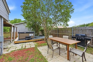 A backyard with a wooden deck, a hot tub, a barbecue grill, and a table with chairs.