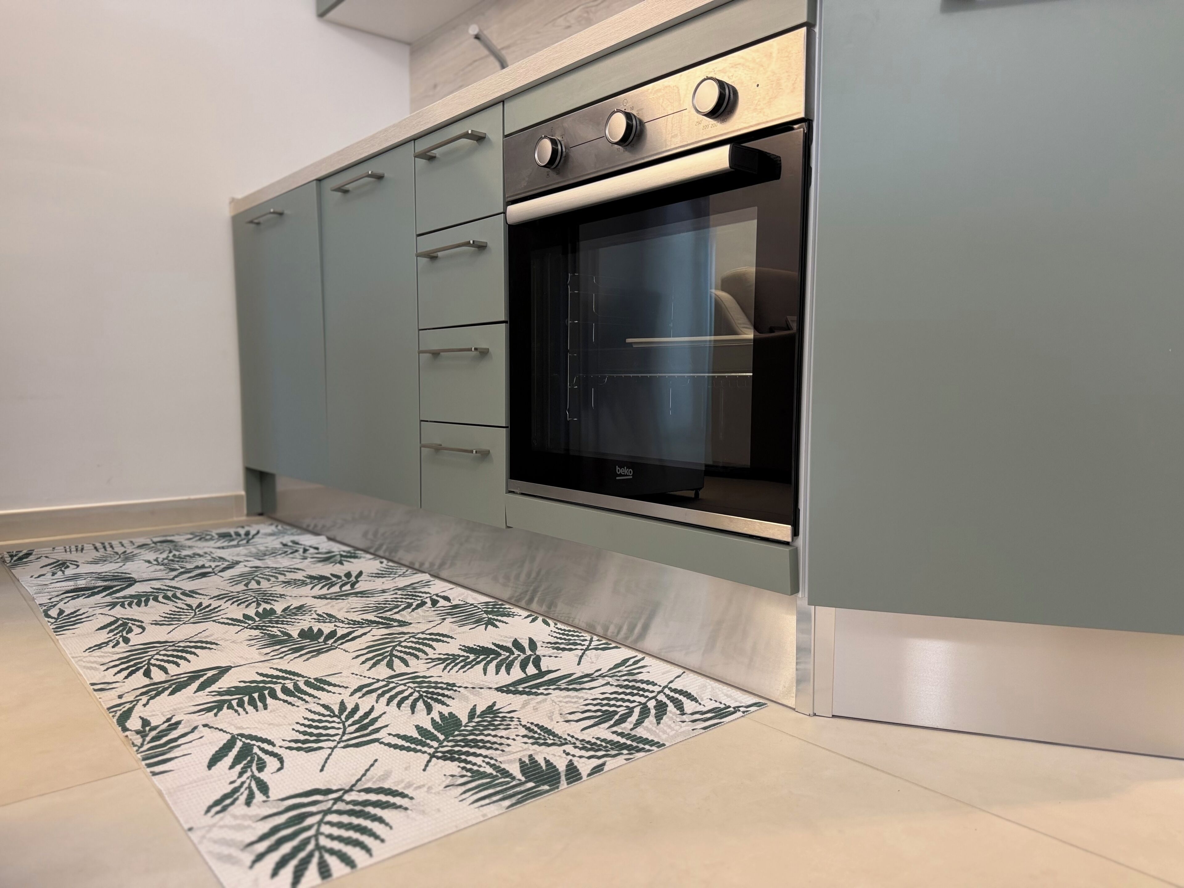 Una cocina con horno empotrado, un tapete estampado y armarios de color claro.