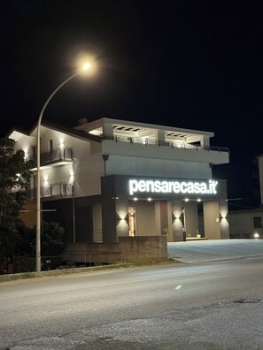 A modern building with a prominent sign reading 'pensarecasa.it' at night. - Newly built apartments just a few meters from the ocean (Campora San Giovanni)