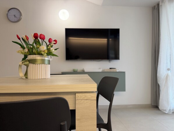 Una sala de estar moderna con una mesa de comedor de madera, una silla negra, un televisor en la pared y un jarrón de flores.