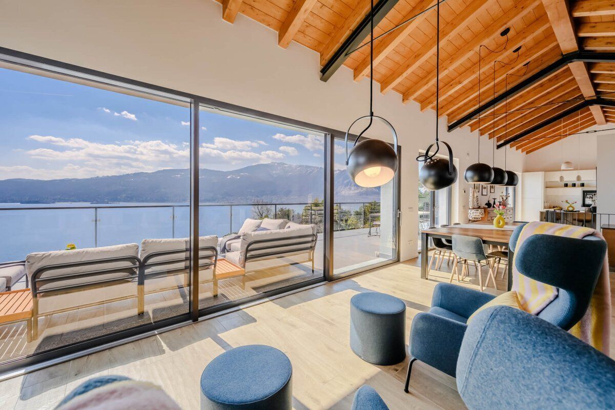 Un intérieur moderne avec une grande baie vitrée, un coin repas et une vue sur un lac et des montagnes.