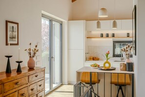 Una cucina moderna con zona pranzo, caratterizzata da una porta scorrevole in vetro, lampade a sospensione e un mobiletto in legno.